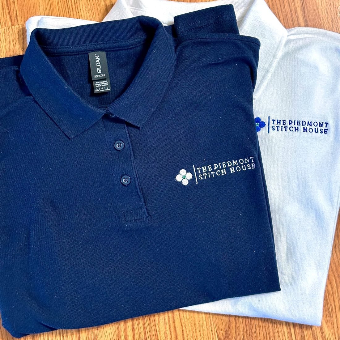 Two embroidered polos stitched with the same logo specification, navy and light blue